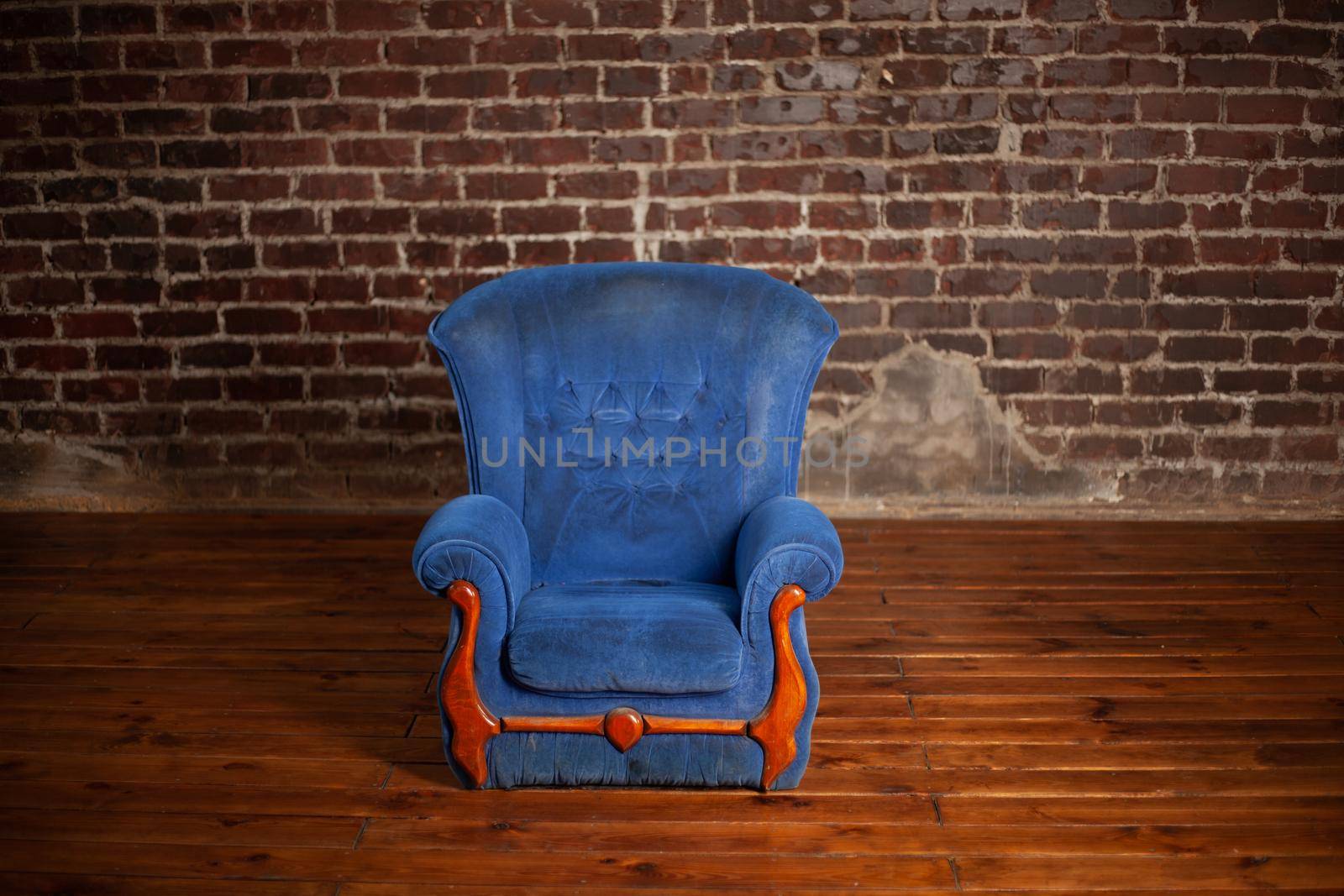 Old dirty vintage blue armchair standing indoor with red brick wall on background
