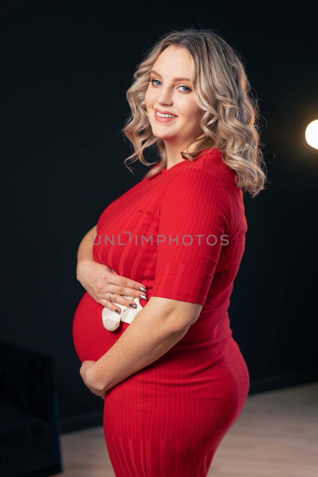 Pregnant Woman Posing In An Elegant red Dress indoors studio black wall background Blonde caucasian middle age female six month pregnancy