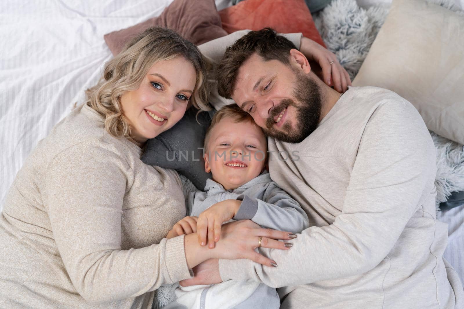 Happy family concept Mother father and little son have fun at home Caucasian family indoors Pregnant mom beard dad and funny little boy lie on the couch