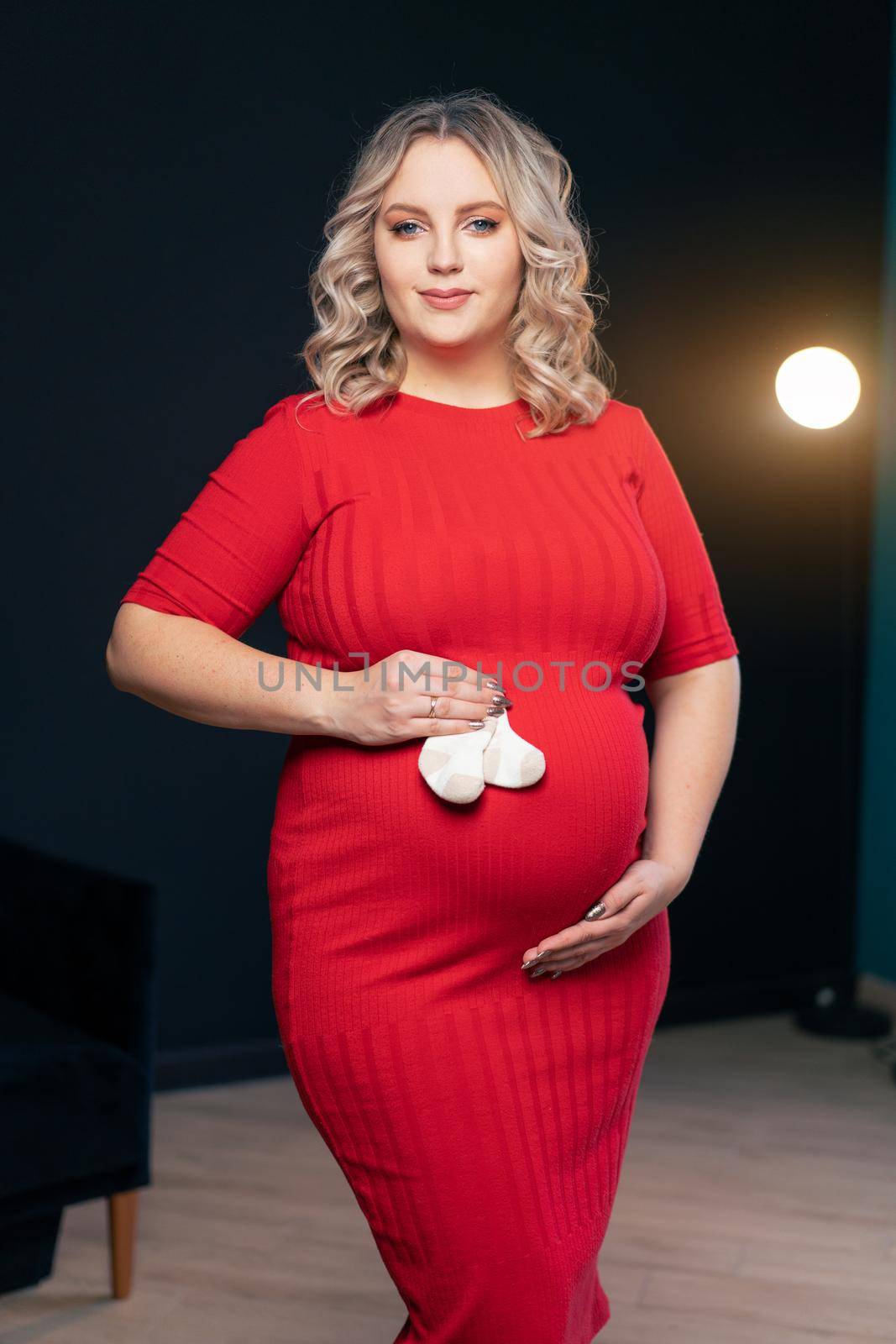 Pregnant Woman Posing In An Elegant red Dress indoors studio black wall background Blonde caucasian middle age female six month pregnancy