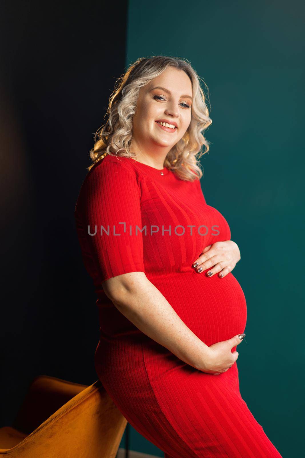 Pregnant Woman Posing In An Elegant red Dress indoors studio black wall background Blonde caucasian middle age female six month pregnancy