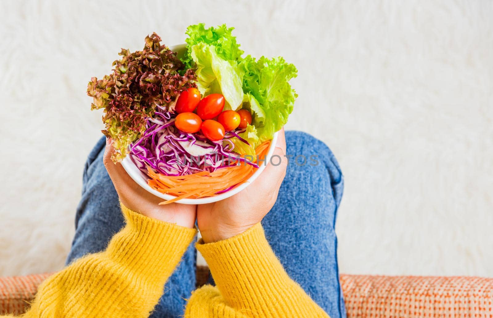 Top view of female hands holding bowl with green lettuce salad on legs, a young woman eating fresh salad meal vegetarian spinach in a bowl, Clean detox healthy food concept