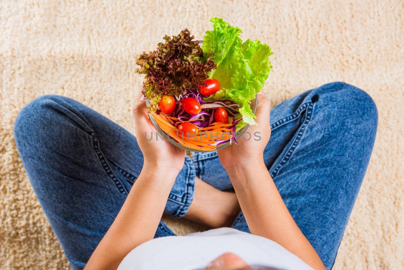 Female hands holding bowl with green lettuce salad on legs, Above young woman eating fresh salad meal vegetarian spinach in a bowl, Clean detox healthy homemade food concept