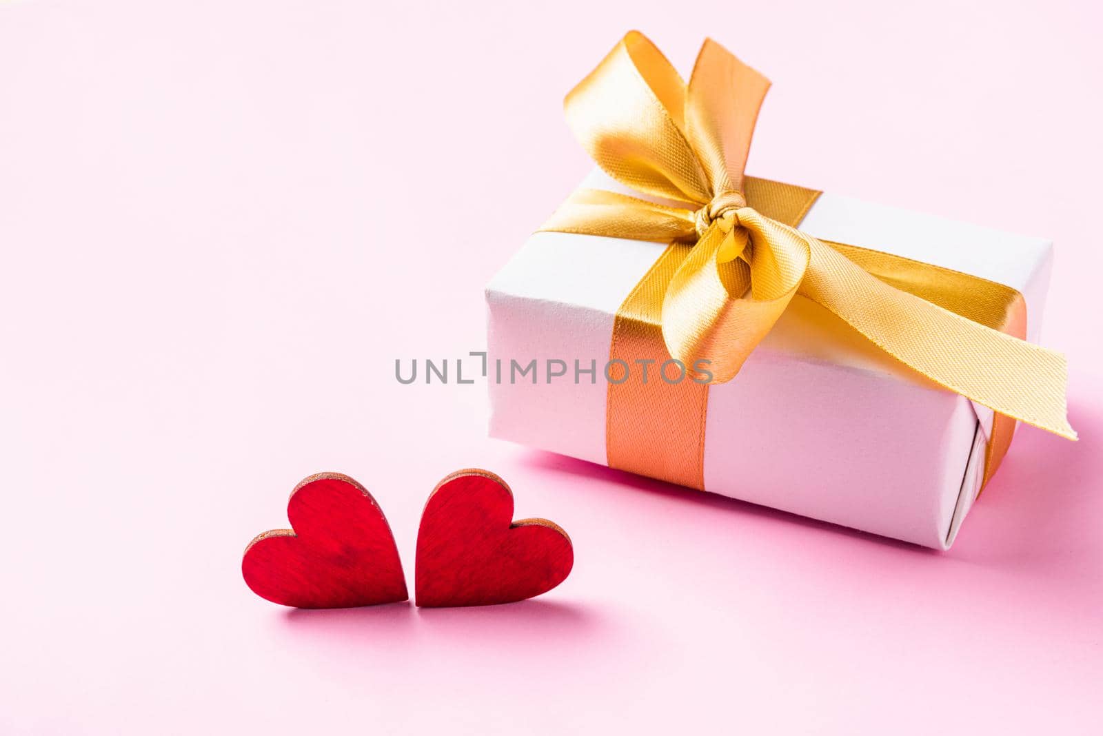 Valentines' day background concept. White gift box with a golden bow ribbon and wood red hearts composition greeting card for happy love isolated on pink background with copy space. View from above