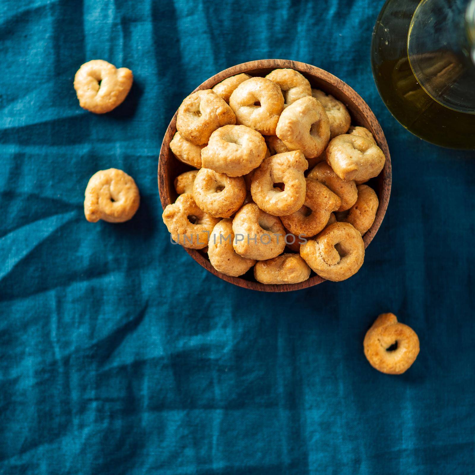 Traditional italian snack taralli or tarallini in wooden bowl over dark blue linen napkin background. Rustic shot of taralli appetizer with copy space. Top view or flat lay. Square crop