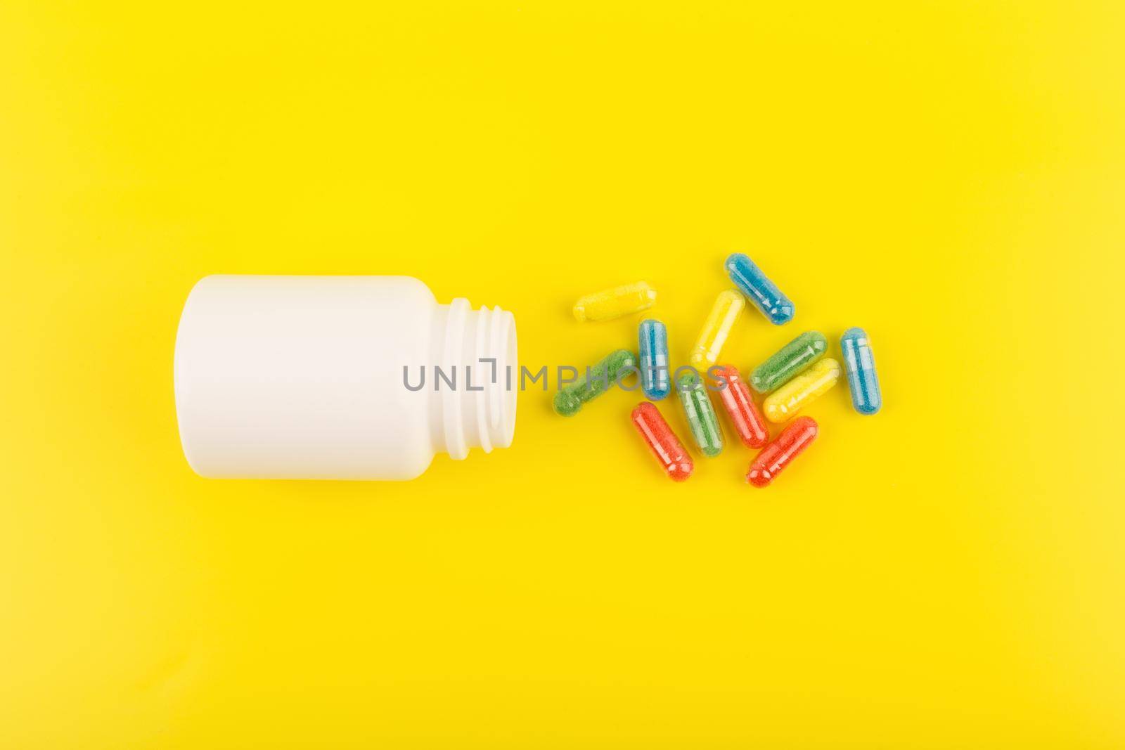 Flat lay with white medication bottle with spilled multicolored pills against yellow background. Concept of vitamins for kids or pharmacy and healthcare