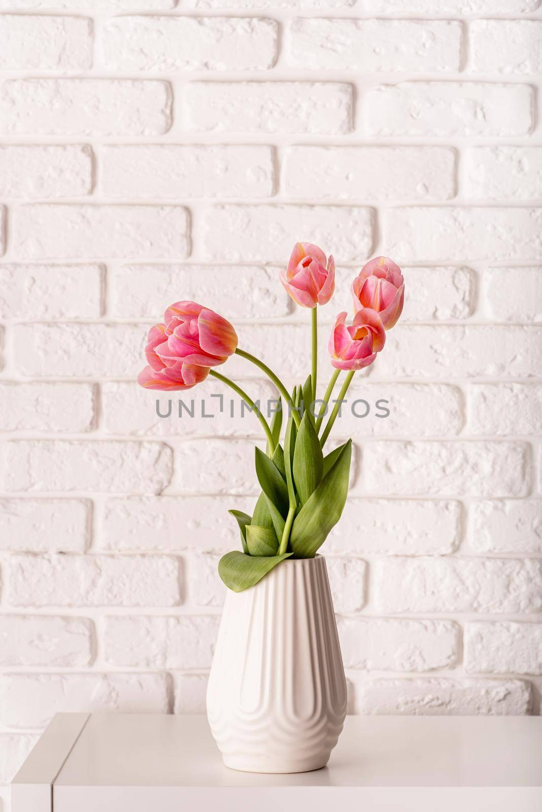 White vase with bouquet of beautiful tulips on brick wall background by Desperada