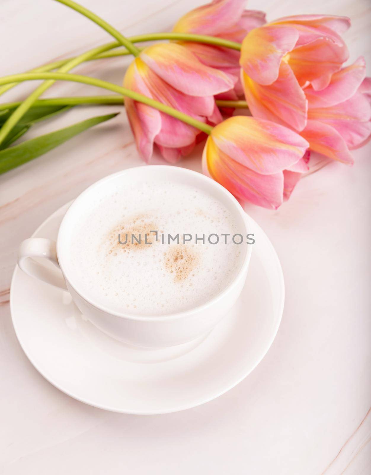 Cup of cappuccino and pink tulips on marble background