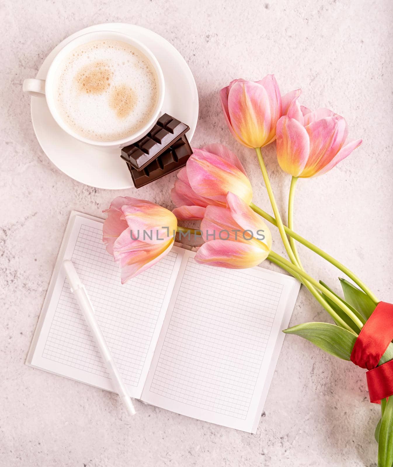 Cup of cappuccino, notebook and pink tulips top view on marble background