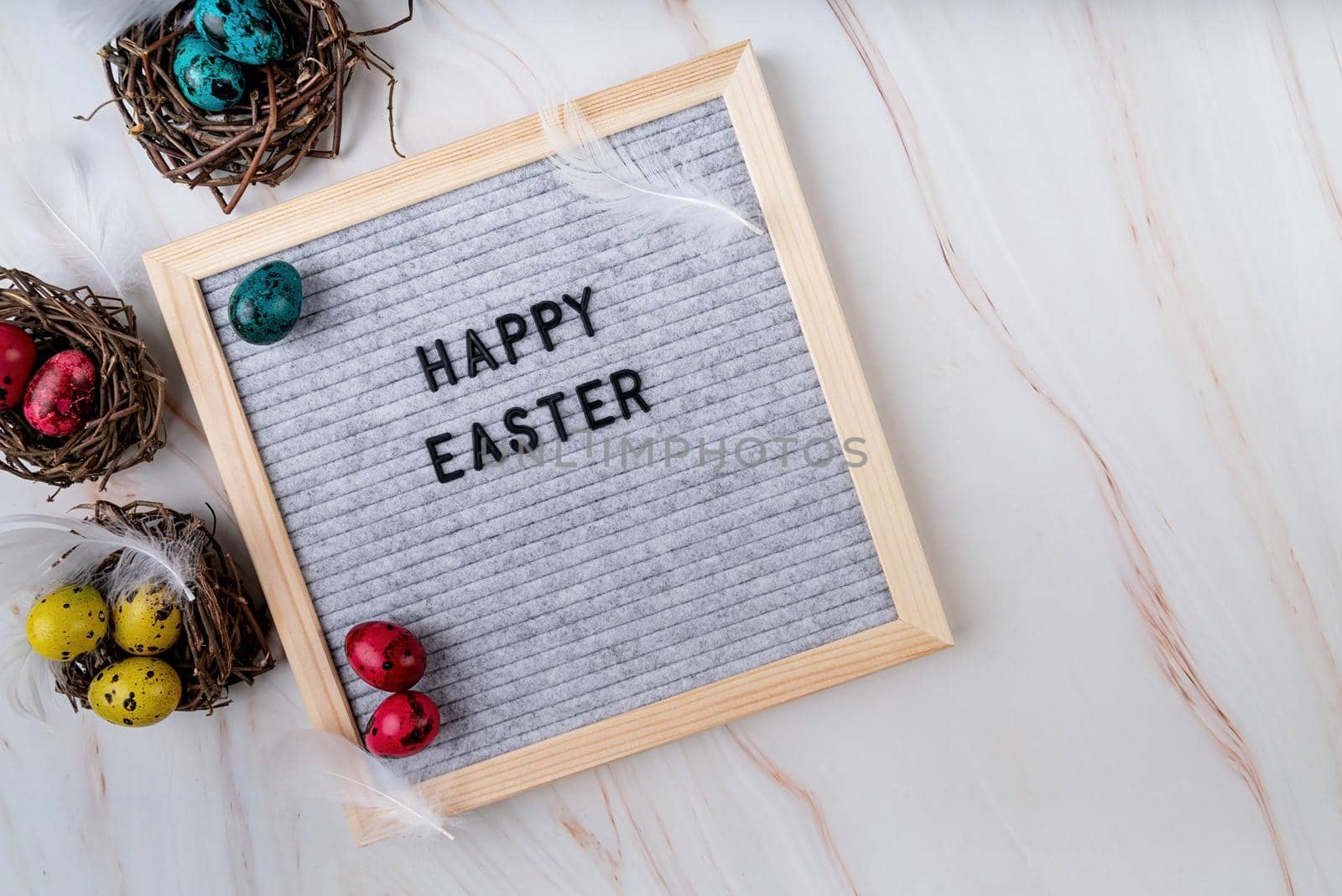 Easter holiday concept. The words Happy Easter on grey felt letter board decorated with quail and chicken eggs and feathers on marble background top view