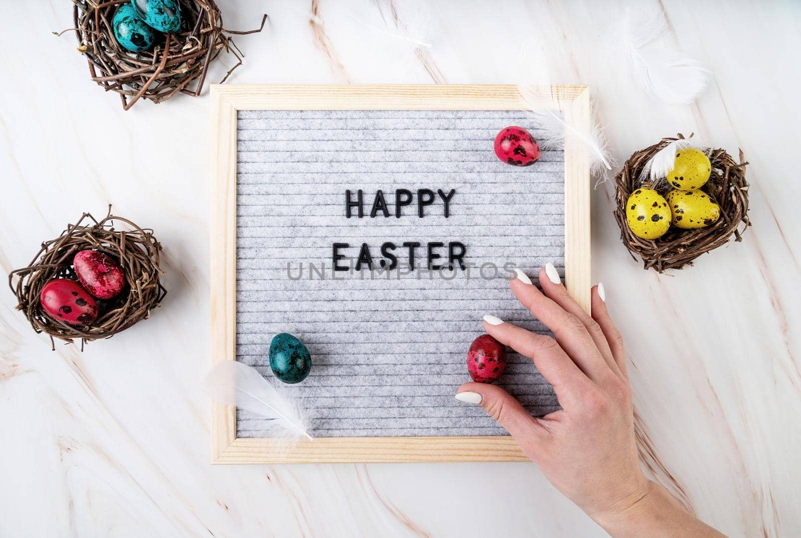 Easter holiday concept. Woman hand putting a colored quail egg on the felt letter board with the words Happy Easter top view flat lay