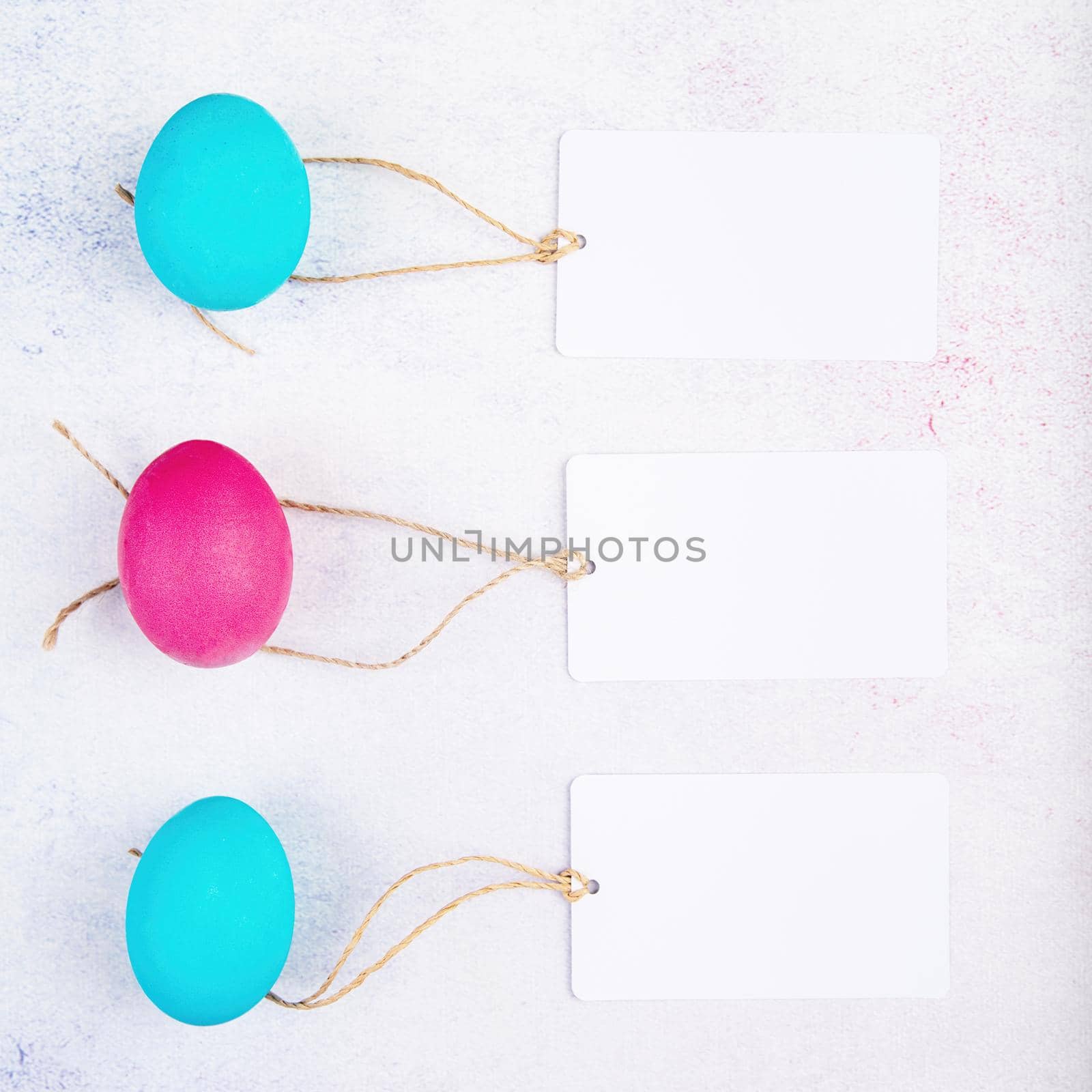 Easter concept. White blank label tags on pink and blue colored eggs top view flat lay