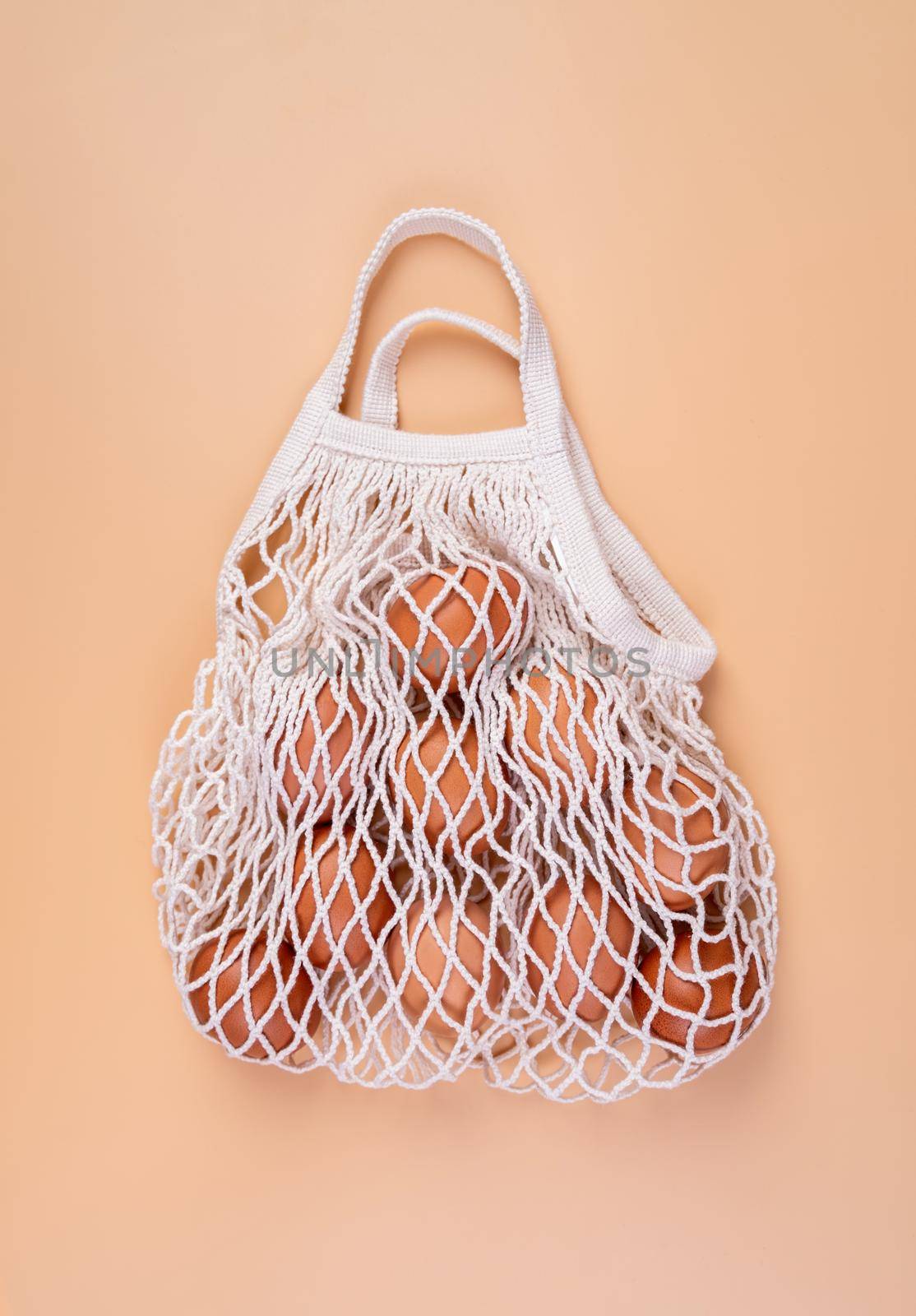 Eggs in a white shopping net bag isolated on beige background top view flat lay by Desperada