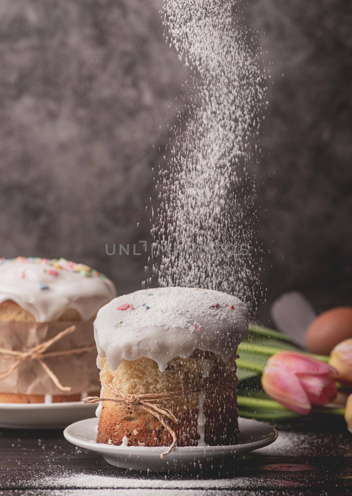 Easter concept. Baking and cooking. Sugar powder falling on glazed easter cake on dark rustic background