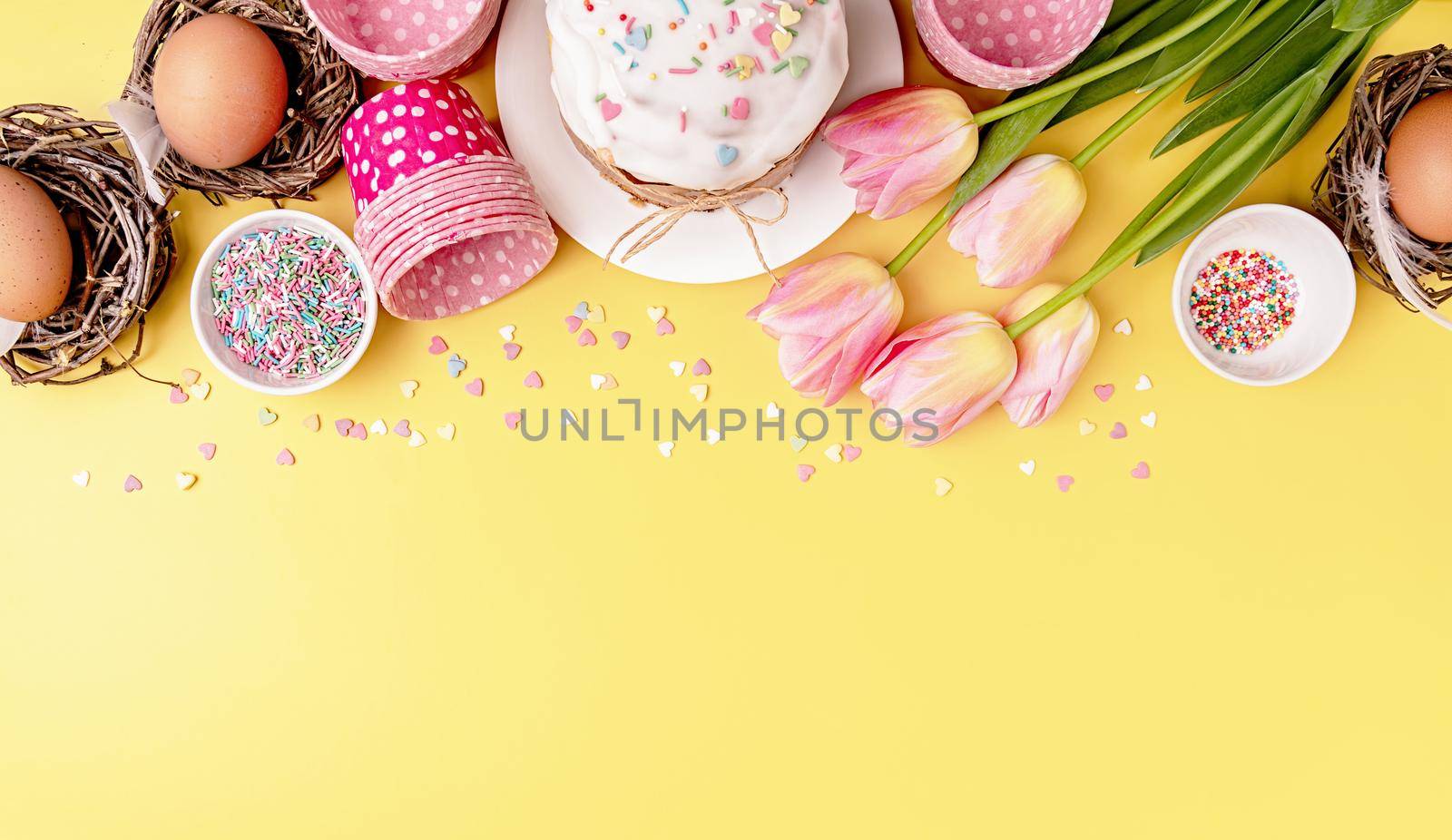 Easter cake with tulips, eggs and baking items top view on yellow background with copy space by Desperada