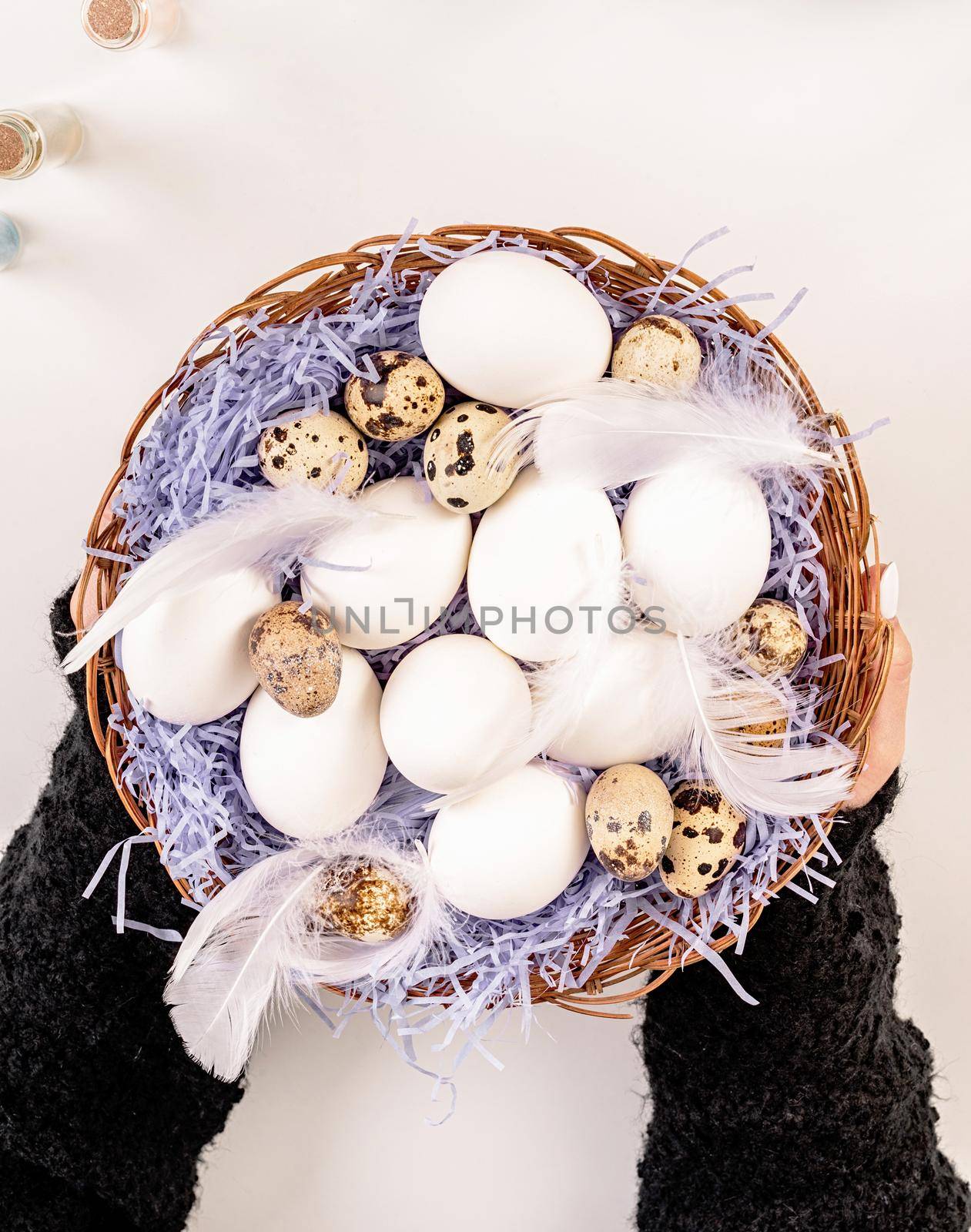 Woman hands holding a big basket with eggs and feathers by Desperada