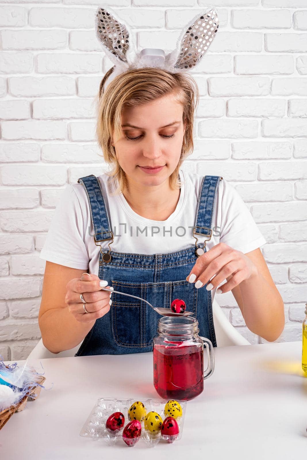 Easter holiday concept. Pretty woman with bunny ears putting Easter quail eggs into mason jar