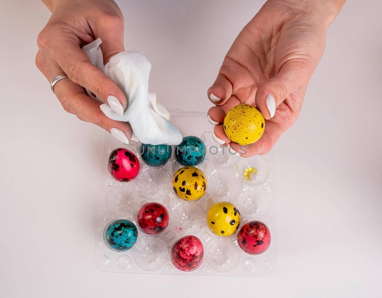 Woman hands coloring Easter quail eggs on white table by Desperada