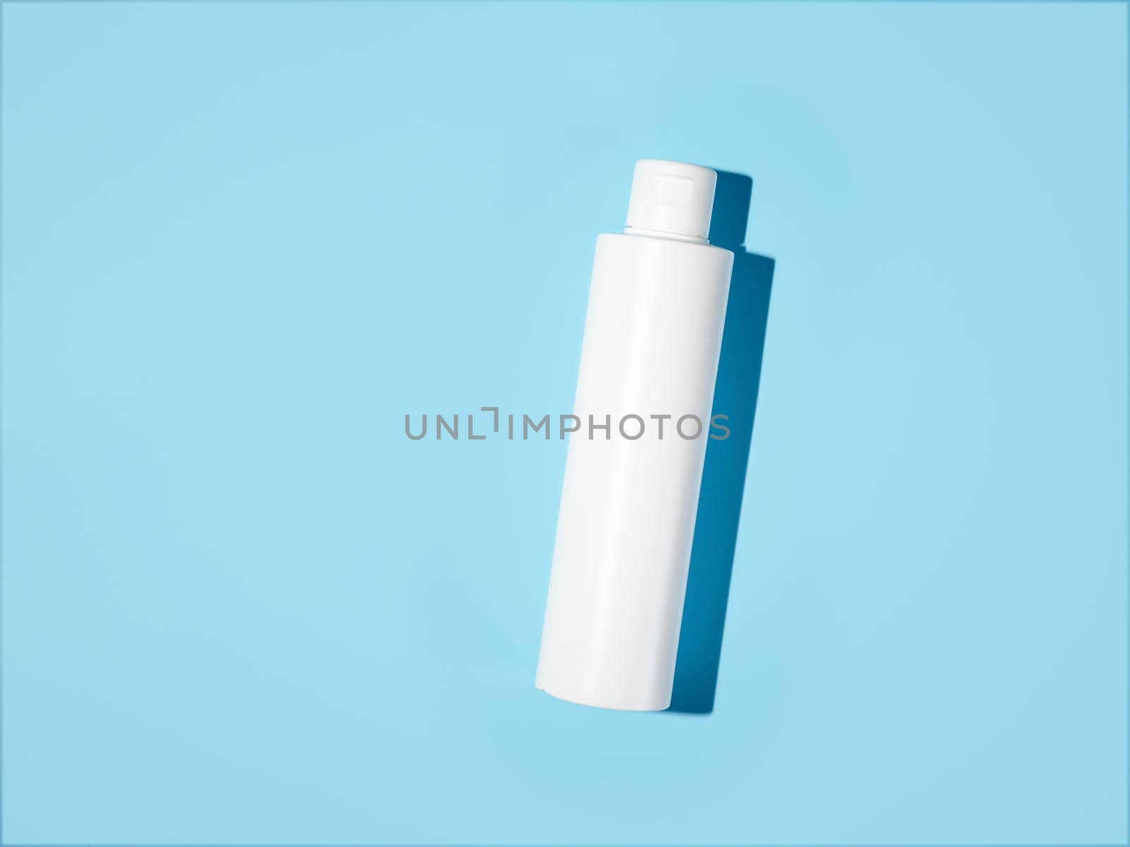 Empty white plastic bottle mockup in hard light. Top view or flat lay. Blank opaque bottle without packaging on blue background. Mock up for package design