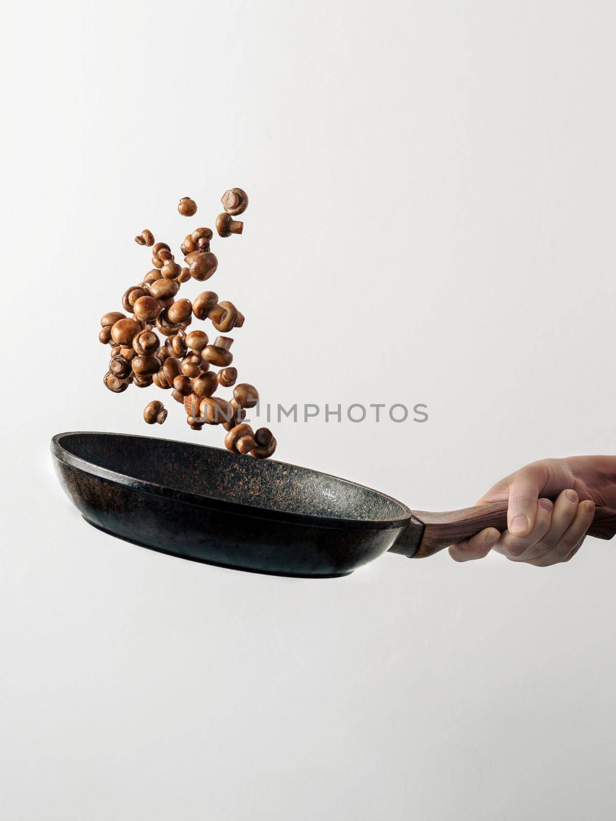 Chef woman preparing mini champignons in skillet frying them. Flying ingredients over pan, copy space. Hotel and caternig business, restaurant menu, book of recipes concept. White background. Vertical