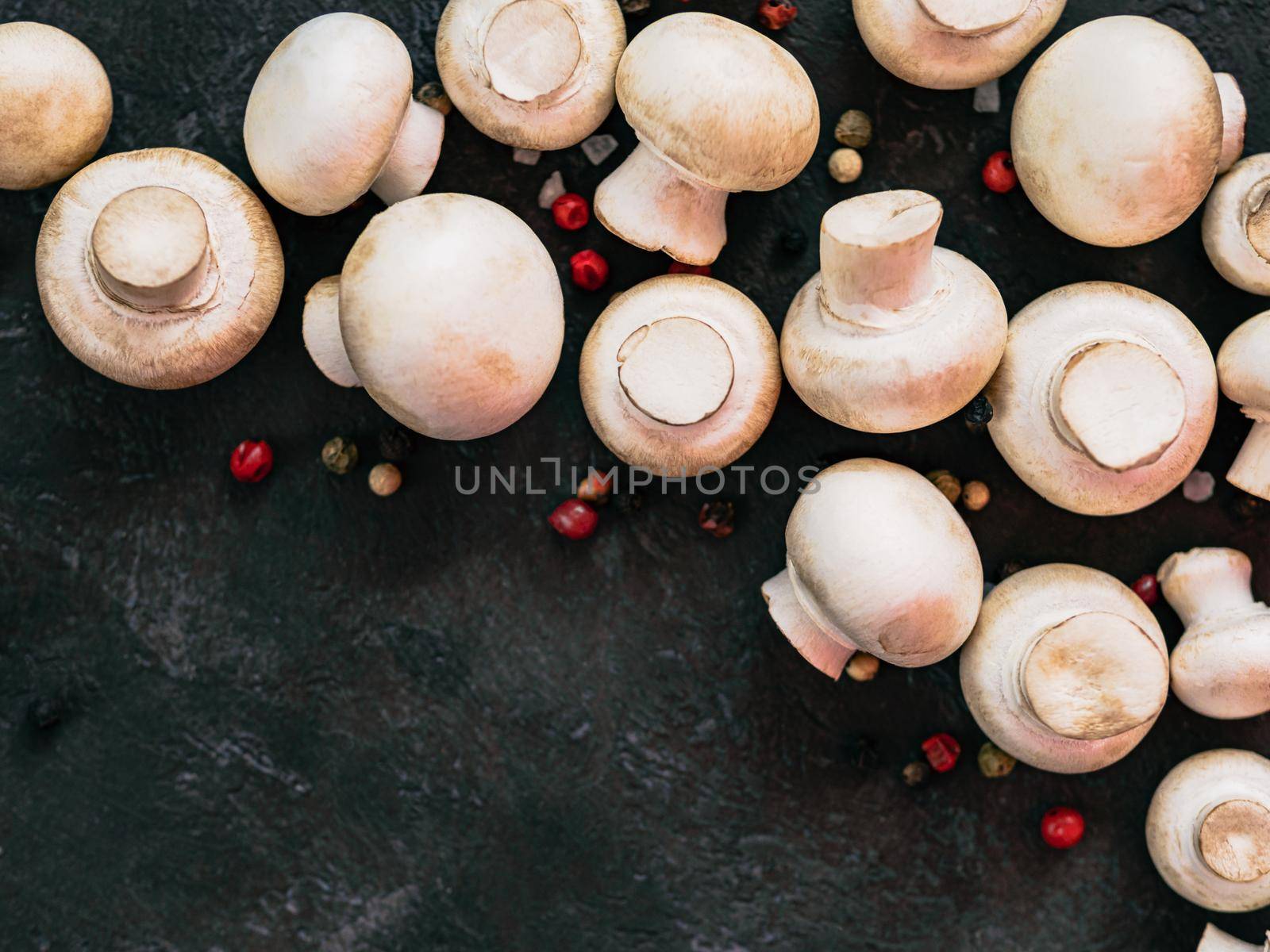Mini champignons with copy space on left edge. Raw whole mushrooms on black background, copy space. Top view or flat lay.