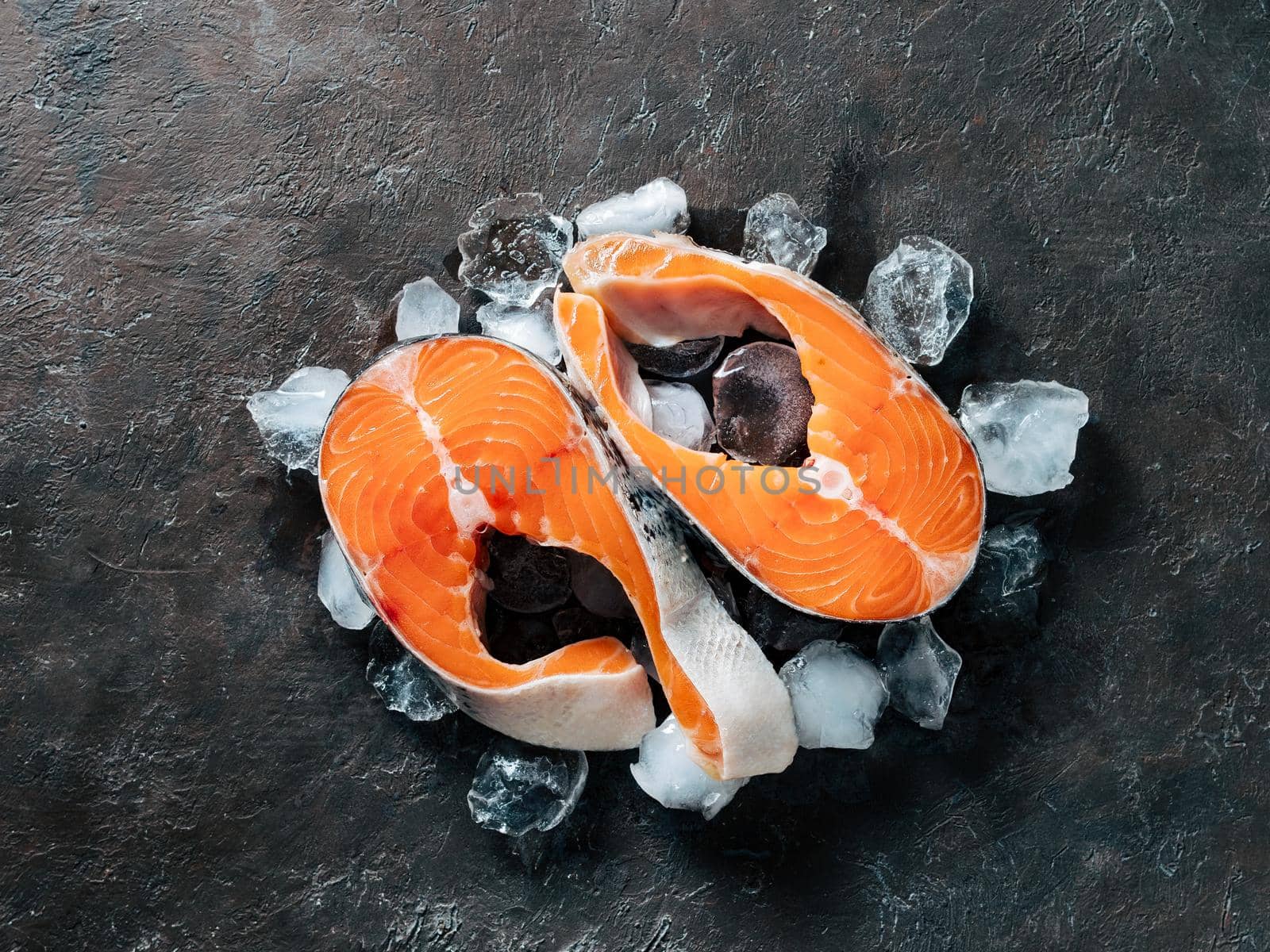 Two raw wild salmon steaks on ice over black textured background. Salmon steaks top view or flat lay.
