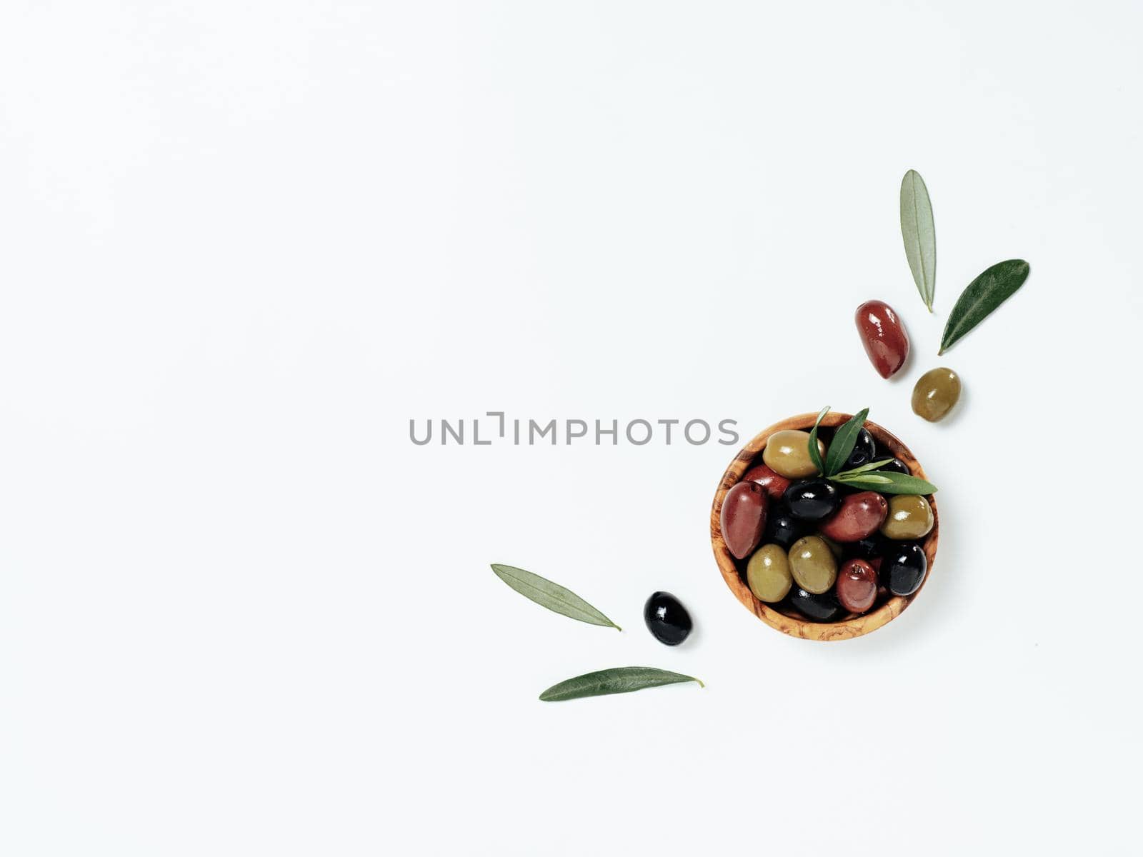 Olives tree leaves and fruits on white background. Small bowl with green, black and red kalamata olives, top view or flat lay. Olives isolated on white with copy space