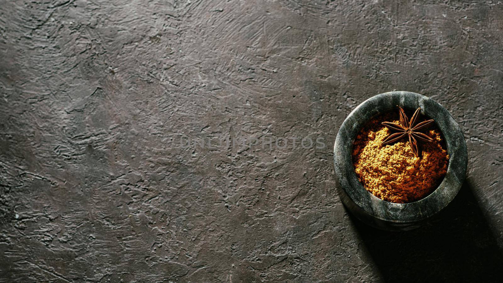 Indian or pakistani masala powder in black marble bowl on black textured background. Small marble bowl with dry curry garam masala mix spices blend with copy space. Top view or flat lay.