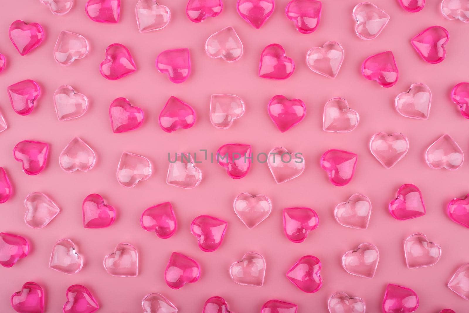 Simple horizontal high angle view pattern with light pink and dark pink glass glossy hearts on pink background. High quality photo