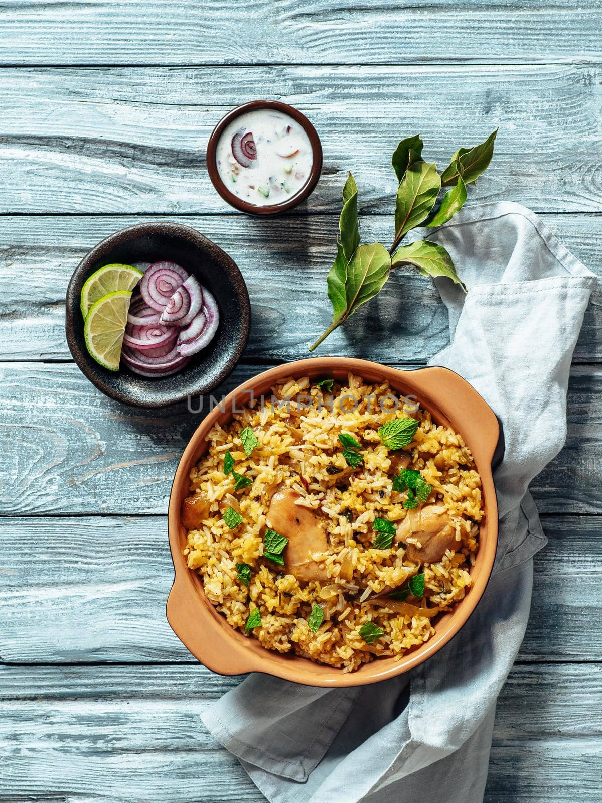 Pakistani food - biryani rice with chicken and raita yoghurt dip. Delicious hyberabadi chicken biryani on gray wooden background. Top view or flat lay. Copy space. Vertical.