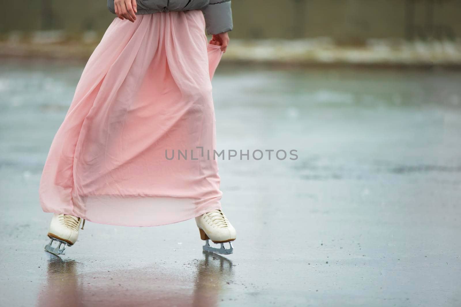 Close-up of female legs on white figure skates in winter at an outdoor ice rink. by Sviatlana