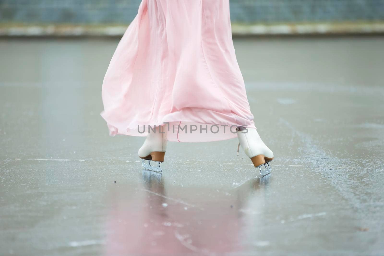 Close-up of female legs on white figure skates in winter at an outdoor ice rink. by Sviatlana