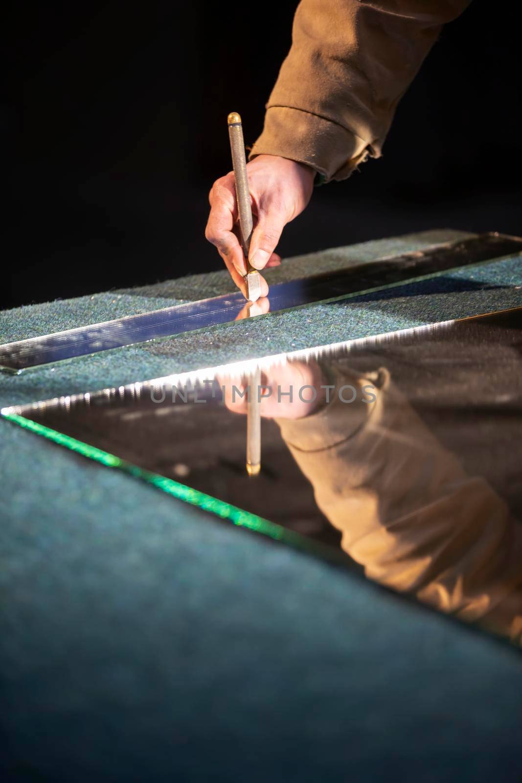 The hand of a working man cuts a mirror with a glass cutter.