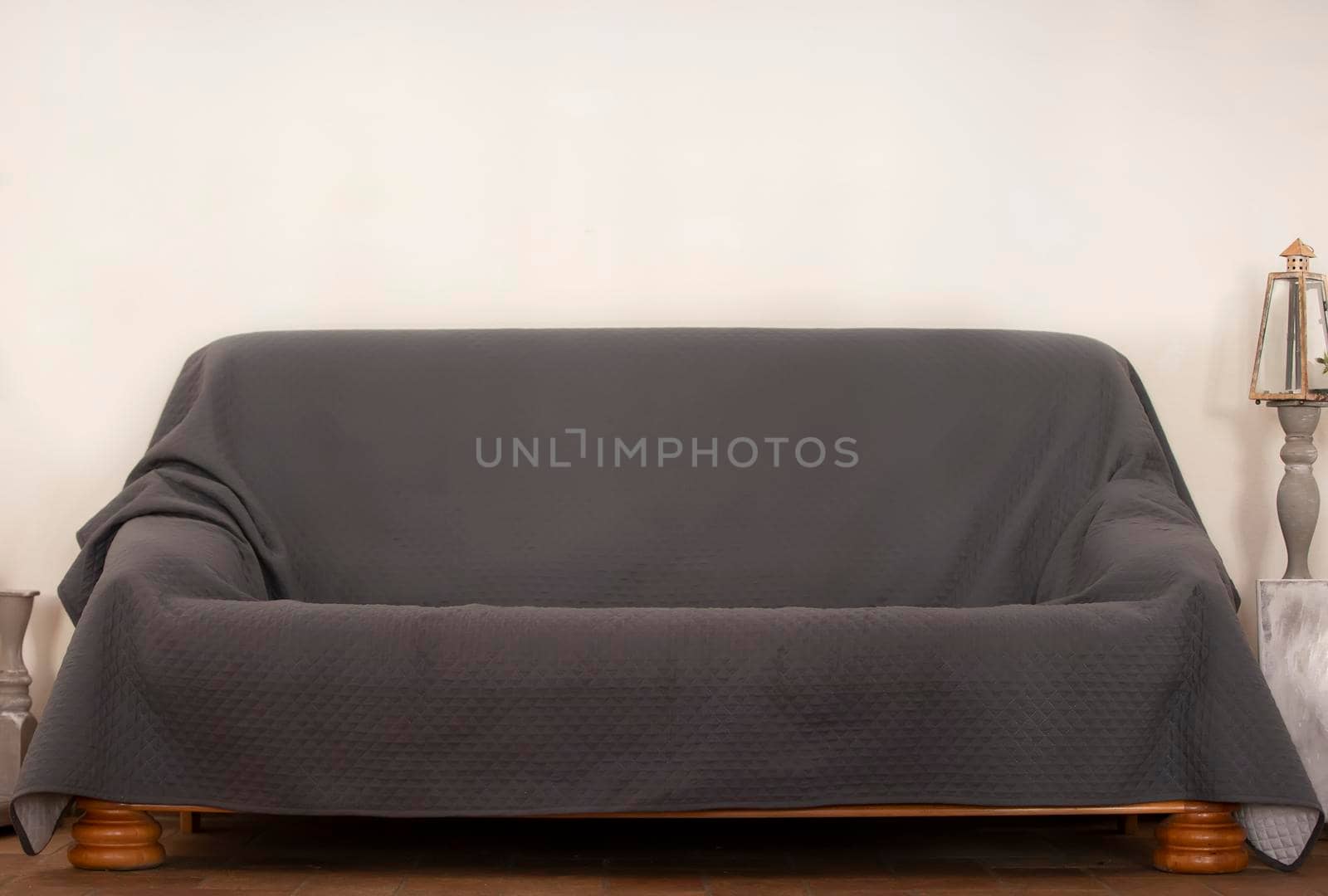 An ordinary sofa covered with gray bedspreads against a beige wall.