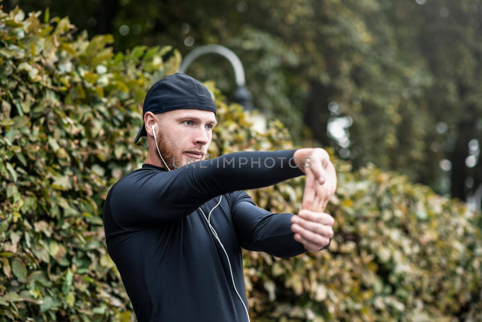 Muscular sportsman stretching out before a sports training at the street in city park