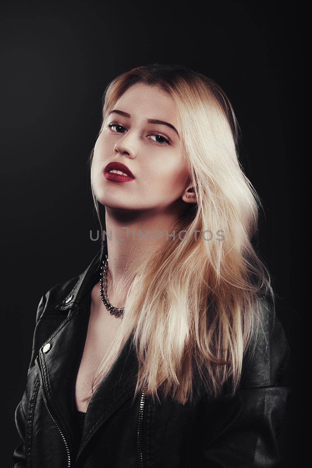 A beautiful, glamour young blond Girl dressed in a black jacket is posing on black background by Nickstock