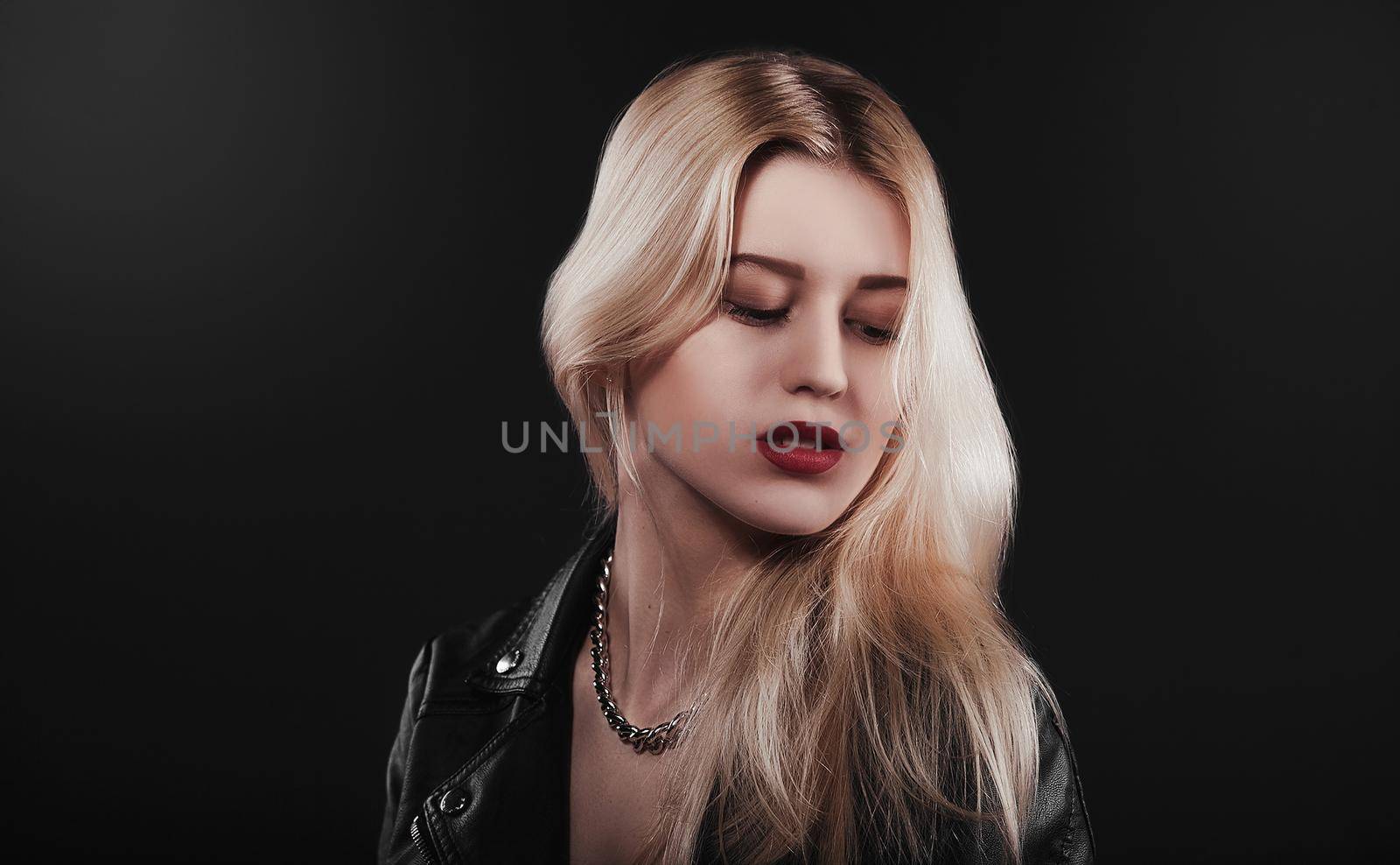 A beautiful, glamour young blond Girl dressed in a black jacket is posing on black background by Nickstock