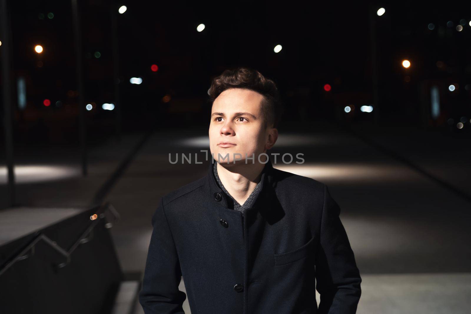 Night time image of confident young and handsome businessman walking along the street with cityscape in the background