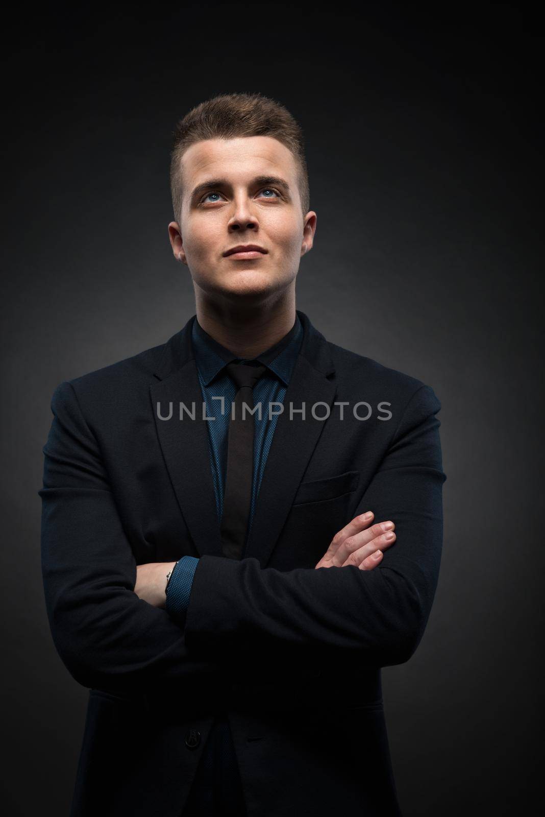 a portrait of a handsome young businessman is thinking and looking up against a black background by Nickstock