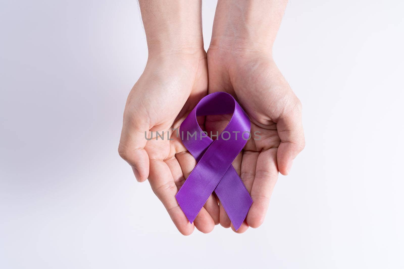 World cancer day, hands holding purple ribbon on grey background with copy space for text. Healthcare and medical concept.