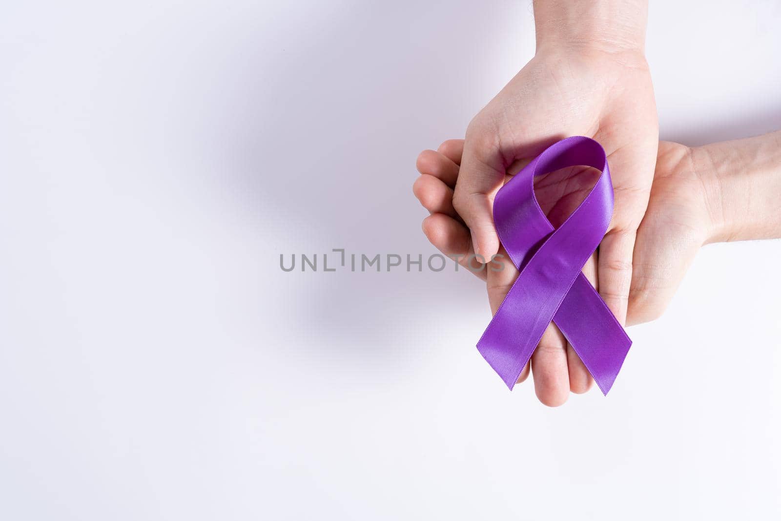 World cancer day, hands holding purple ribbon on grey background with copy space for text. Healthcare and medical concept.