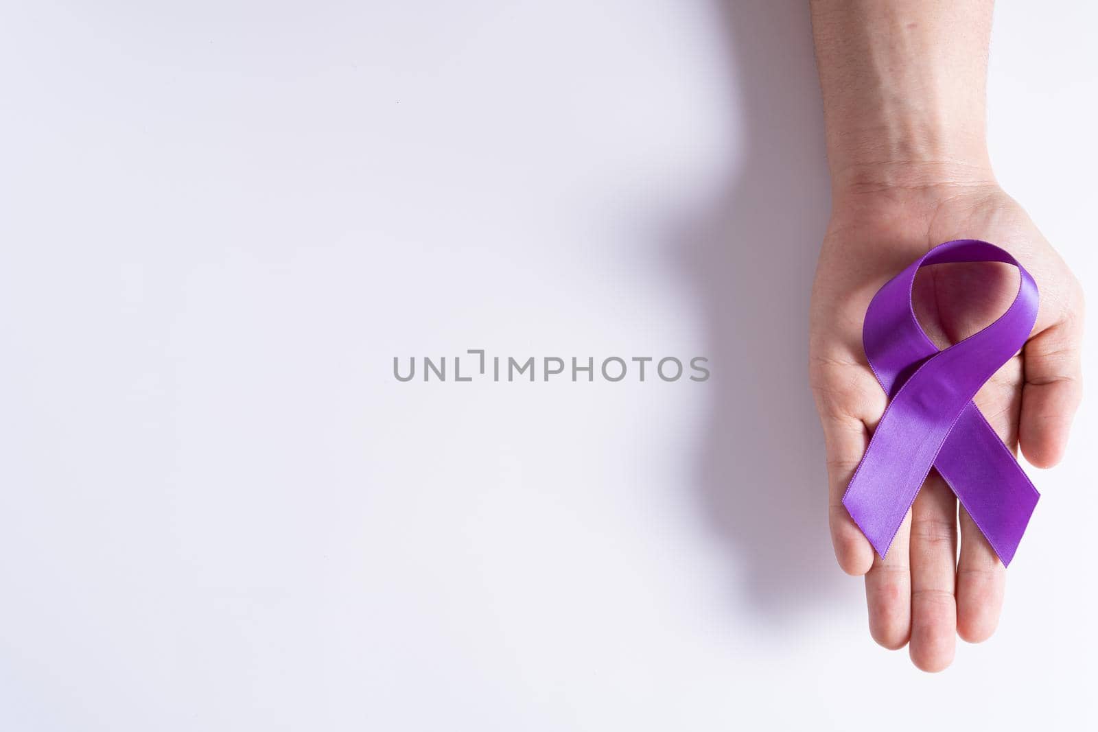 World cancer day, hands holding purple ribbon on grey background with copy space for text. Healthcare and medical concept.