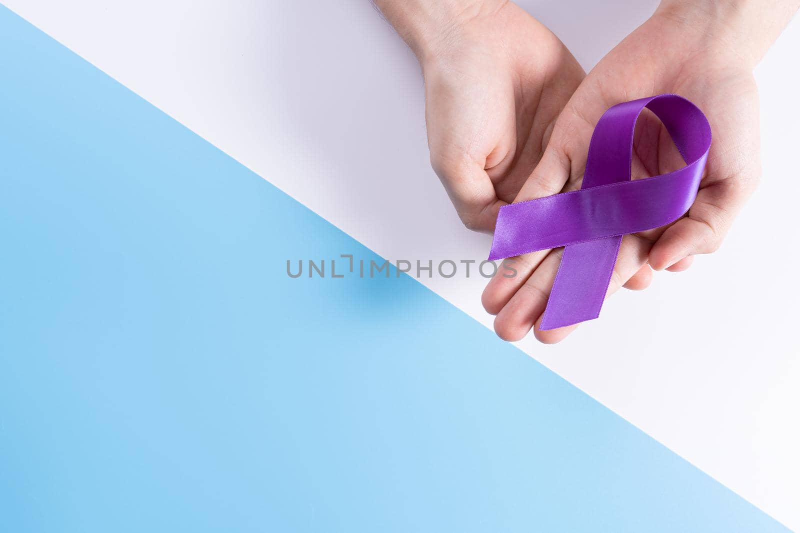 World cancer day, hands holding purple ribbon on with and blue background with copy space for text. Healthcare and medical concept. by mikesaran