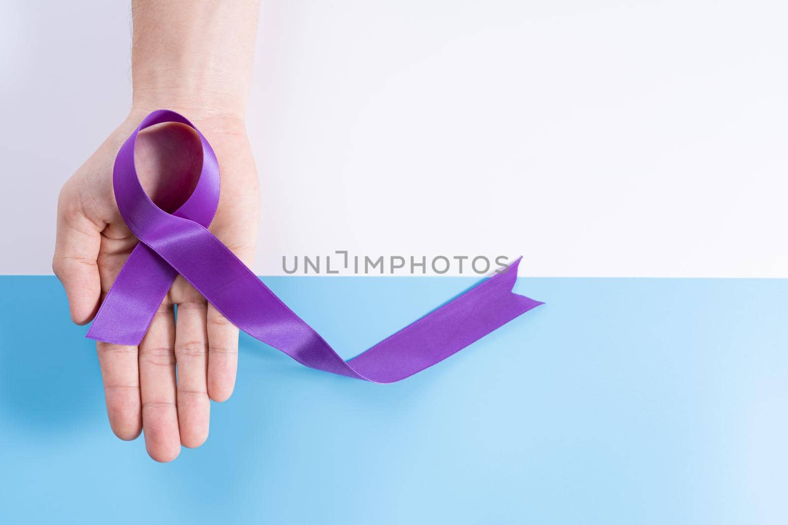 World cancer day, hands holding purple ribbon on with and blue background with copy space for text. Healthcare and medical concept.