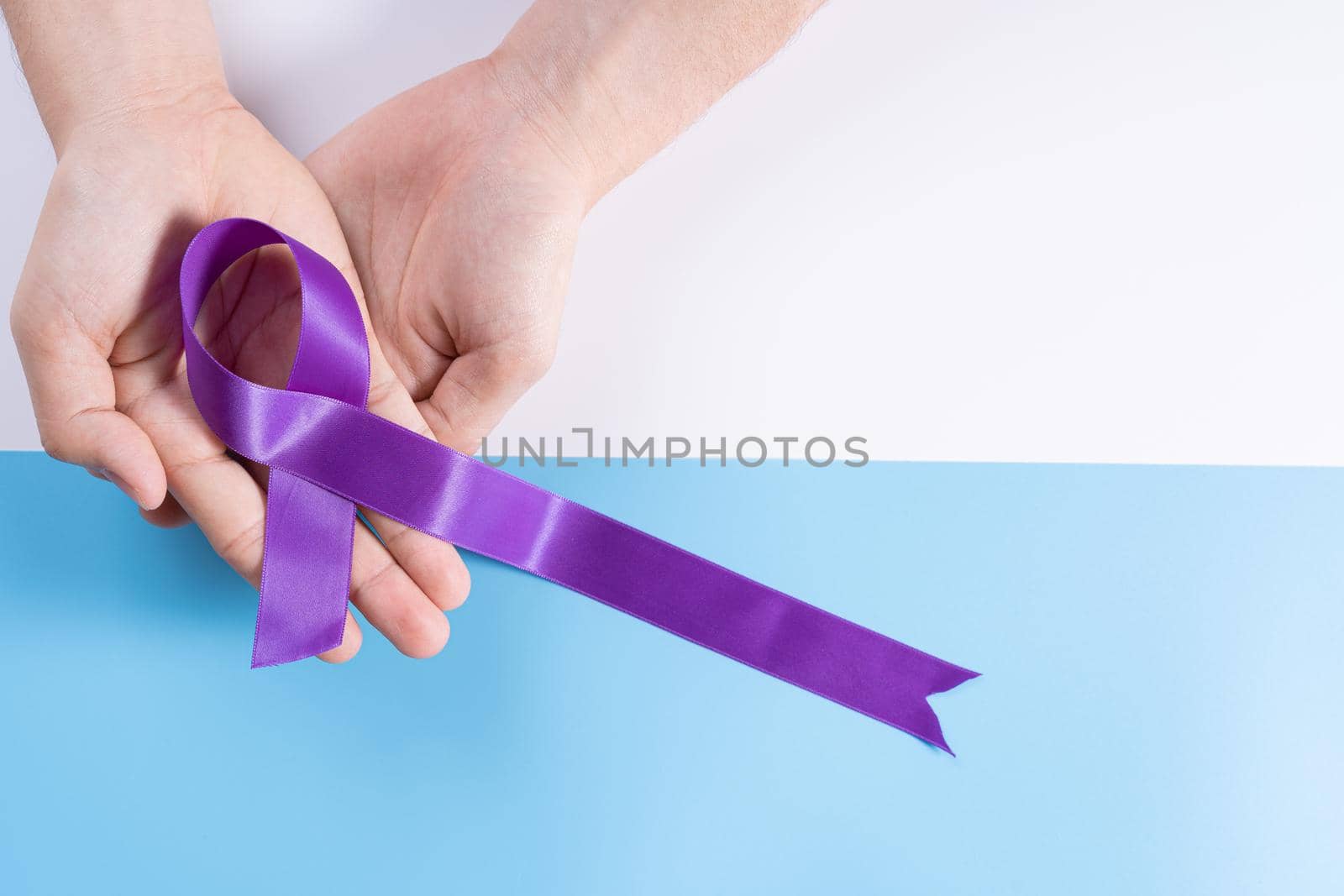 World cancer day, hands holding purple ribbon on with and blue background with copy space for text. Healthcare and medical concept. by mikesaran