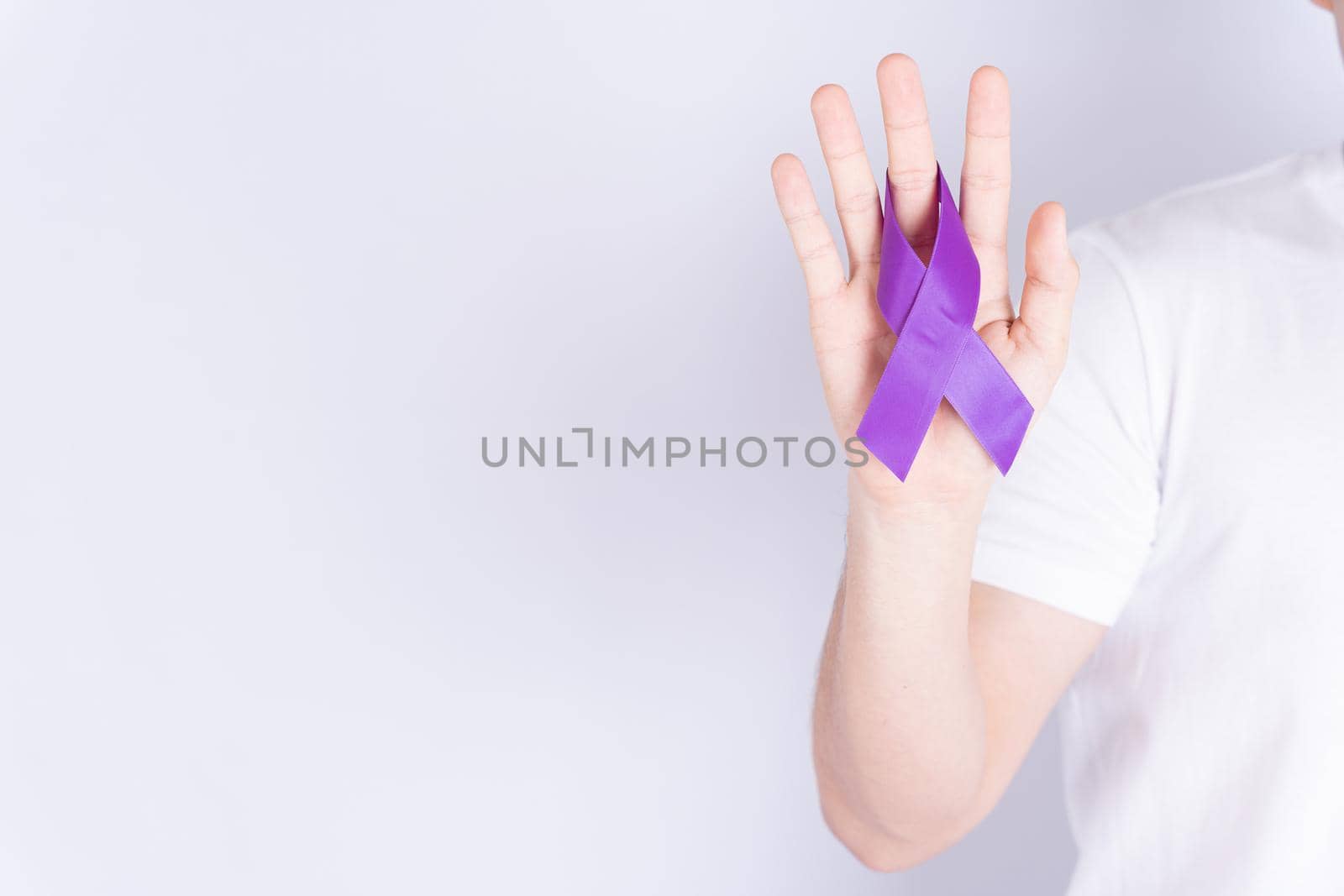 World cancer day, hands holding purple ribbon on grey background with copy space for text. Healthcare and medical concept. by mikesaran