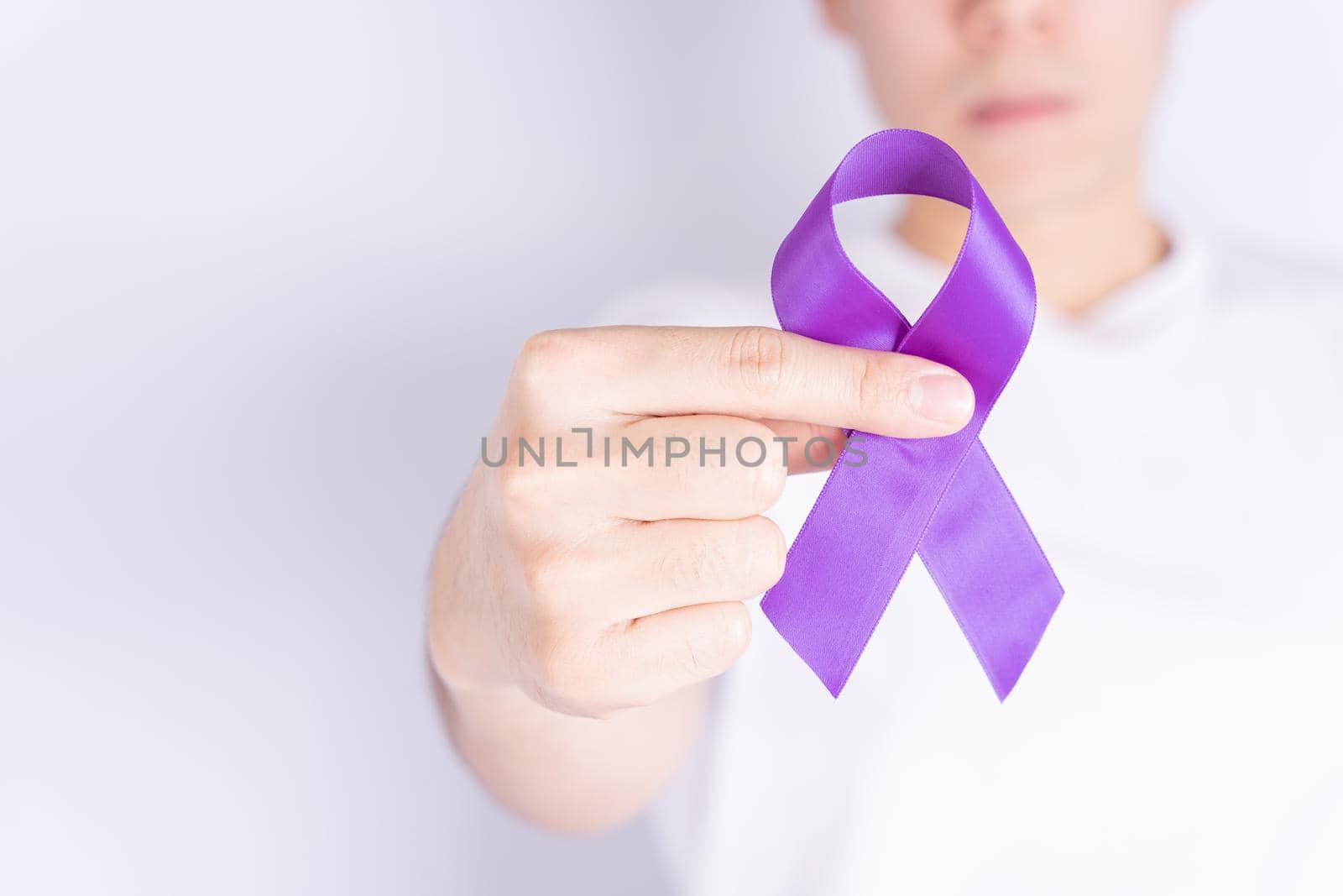 World cancer day, hands holding purple ribbon on grey background with copy space for text. Healthcare and medical concept.