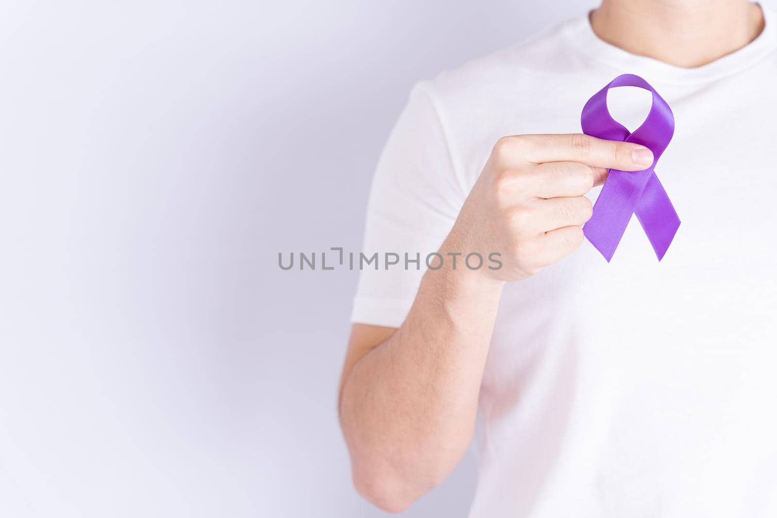 World cancer day, hands holding purple ribbon on grey background with copy space for text. Healthcare and medical concept.