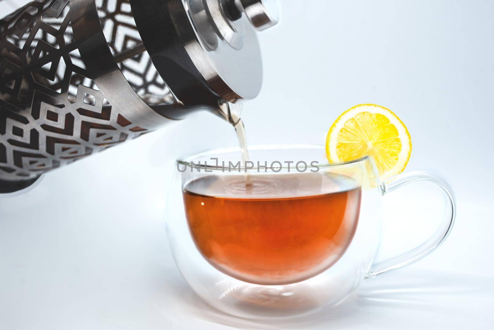 Glass teapot pouring black tea into cup isolated on white