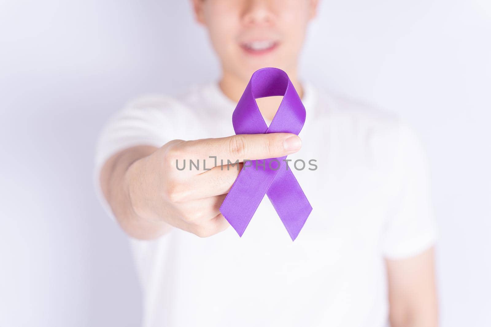 World cancer day, hands holding purple ribbon on grey background with copy space for text. Healthcare and medical concept.